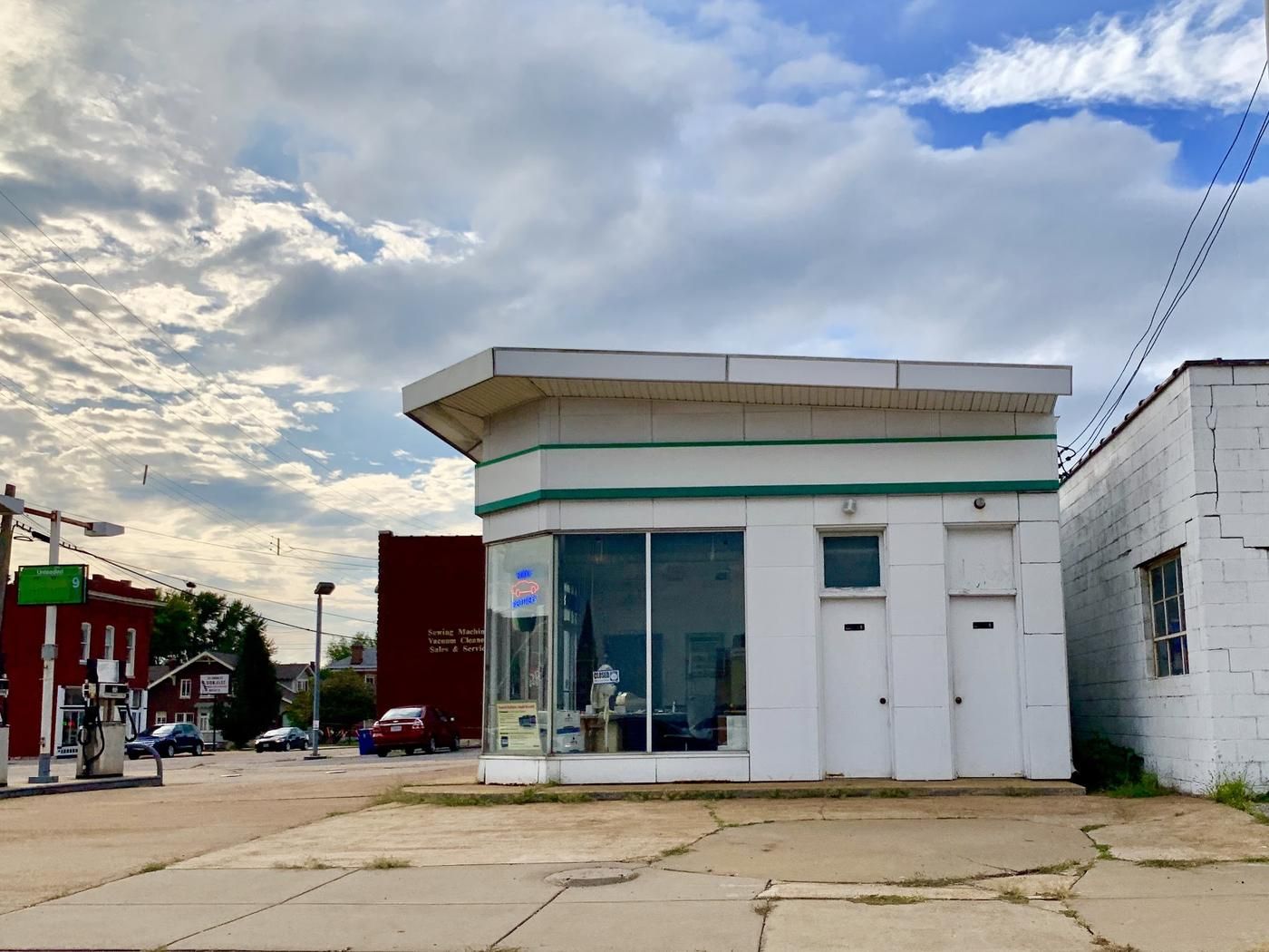 The office end of the Budde Brothers station under a blue sky, white enamel tile with a green band and a neon sign in the window